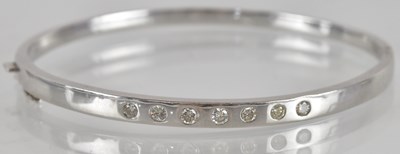 Lot 1574 - An 18ct white gold hinged bracelet, inset with...