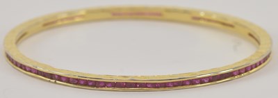 Lot 1310 - A yellow metal ruby set eternity bangle,...