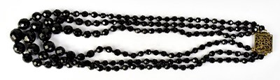 Lot 1095 - A three strand faceted jet bead necklace, with...