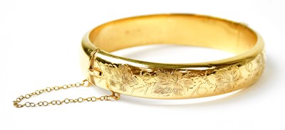 Lot 1079 - A gold-plated hinged bangle with engraved leaf...