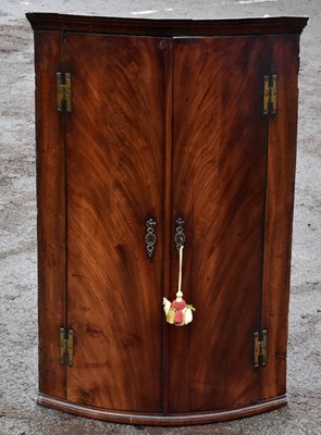Lot 1596 - A Georgian mahogany two door wall hanging bowfronted corner cupboard