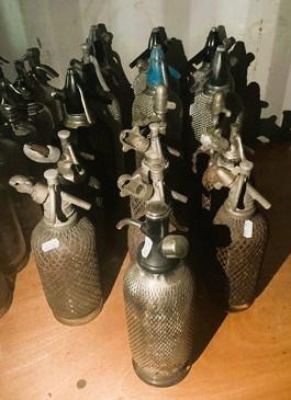 Lot 87 - Sixteen mesh and glass soda syphons with metal...