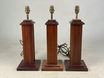 Lot 630 - Three mahogany vertical ribbed table lamps,...