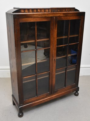 Lot 1111 - A 1920s oak glazed bookcase on bun feet,...