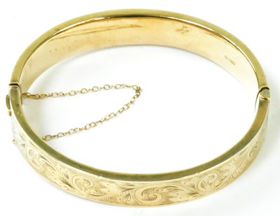 Lot 774 - A 9ct yellow gold hinged bangle with engine...