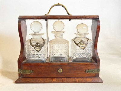Lot 545 - An oak three bottle tantalus with two alcohol...